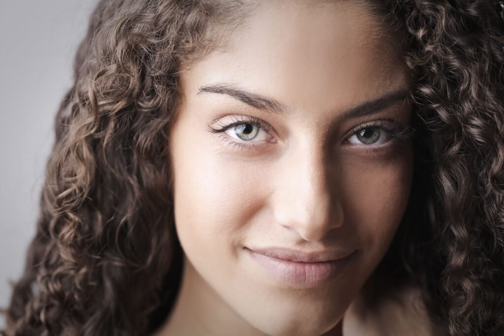 Portrait of a smiling woman with clear skin and curly hair showing results from a skincare routine for combination skin.